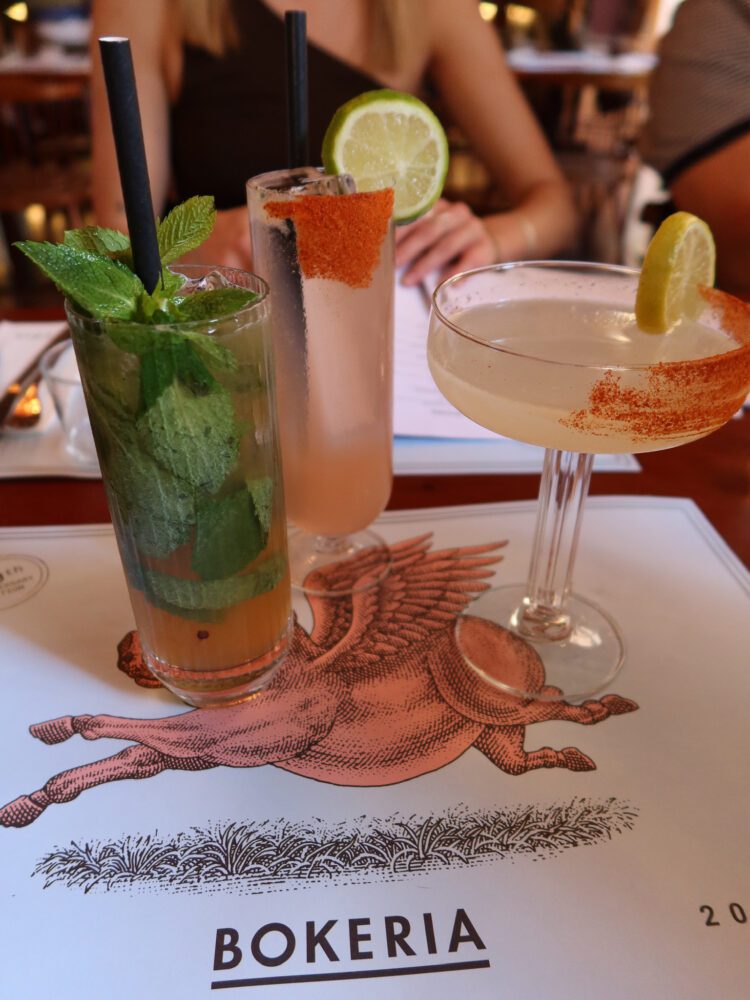 Colorful cocktails served at Bokeria Kitchen & Wine Bar in Split, Croatia—featuring a mint mojito, a chili-rimmed citrus cocktail, and a lime-garnished martini on a placemat with the restaurant’s iconic winged horse logo.