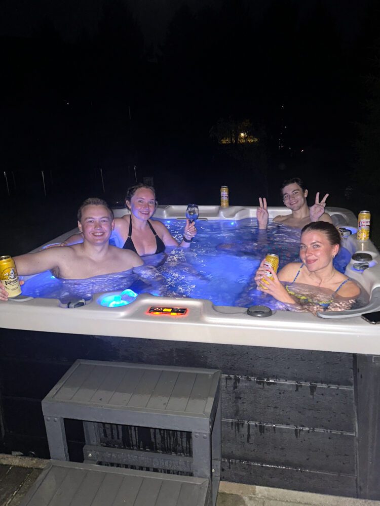 Group of friends enjoying drinks in an illuminated outdoor hot tub at night in Croatia, holding Kozel beer and wine under the stars—capturing a cozy, relaxing moment during a European summer getaway.