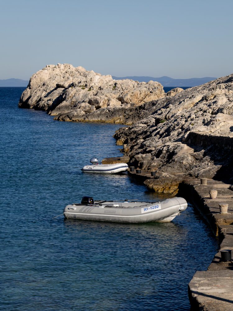 Inflatable boats floating beside a rocky shoreline at Zaraće on Hvar Island, Croatia, with jagged limestone cliffs and calm Adriatic waters under a clear blue sky—showcasing the rugged beauty of the Dalmatian coast.