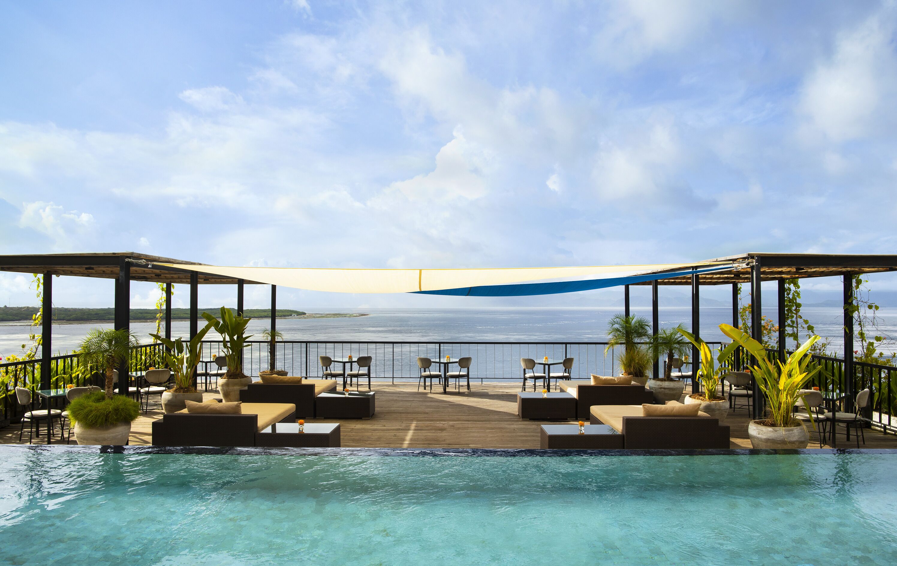 Infinity pool at Adiwana Warnakali Resort overlooking the ocean, with shaded lounge areas and panoramic views of Nusa Penida’s coastline.