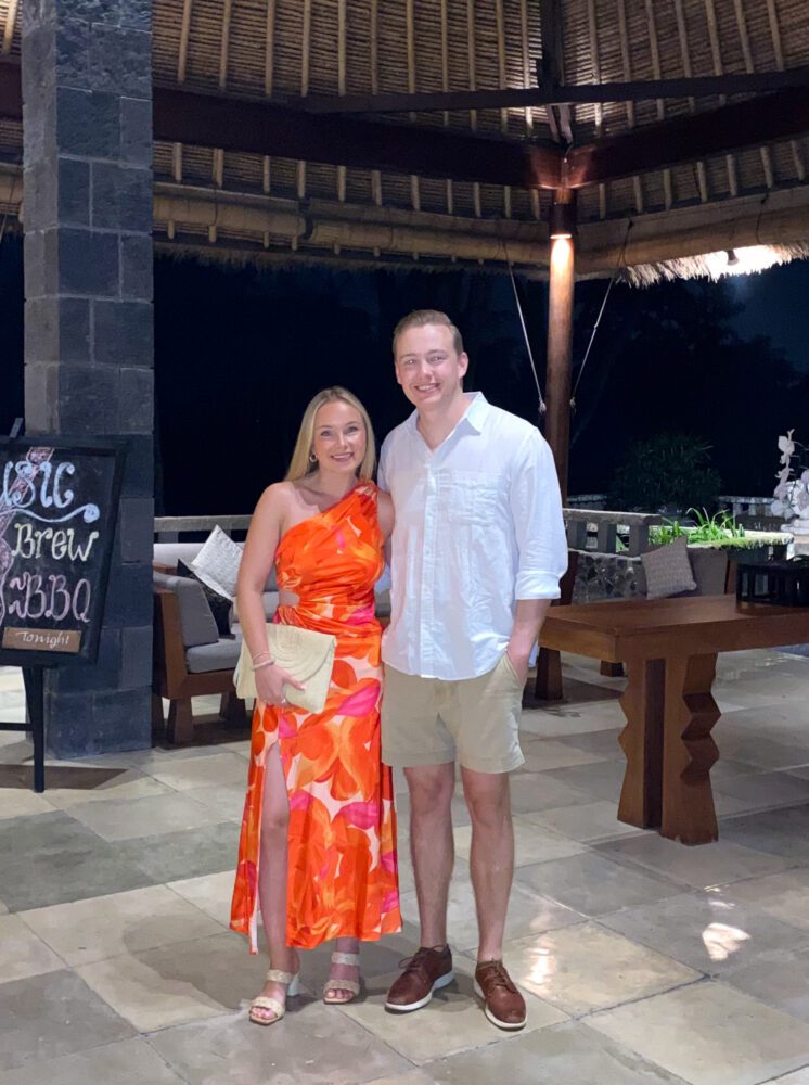 Couple dressed up for dinner at Alila Ubud, standing under a thatched pavilion with BBQ night signage.