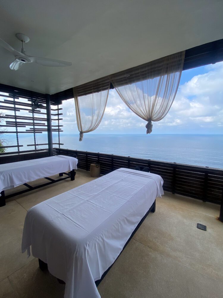 Cliffside open-air spa cabana at Alila Villas Uluwatu, featuring twin massage tables with panoramic views of the Indian Ocean and billowing white curtains for a serene, luxurious wellness experience.