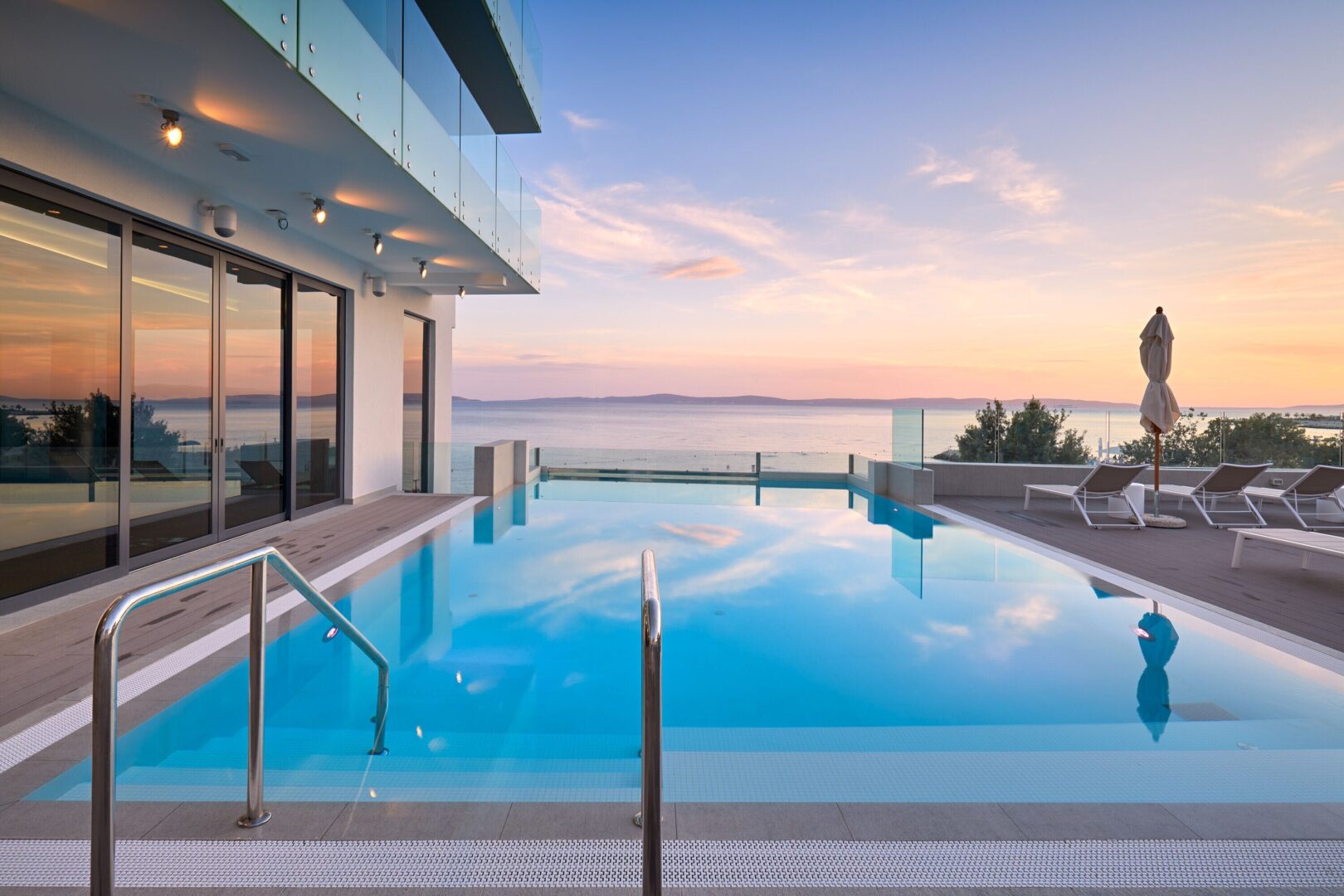 Hotel infinity pool facing the Adriatic Sea at sunset, with soft reflections and tranquil loungers lining the deck.