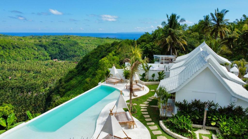 Stunning hilltop infinity pool at Atalaya Villas Nusa Penida, overlooking lush jungle and the distant blue sea with elegant white villas nestled into the tropical landscape.