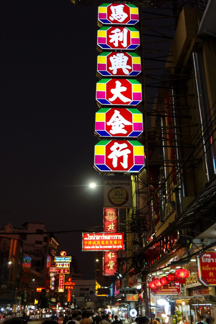Bright neon Chinese signs light up the bustling streets of Bangkok’s Chinatown at night, as crowds weave through food stalls and glowing lanterns.