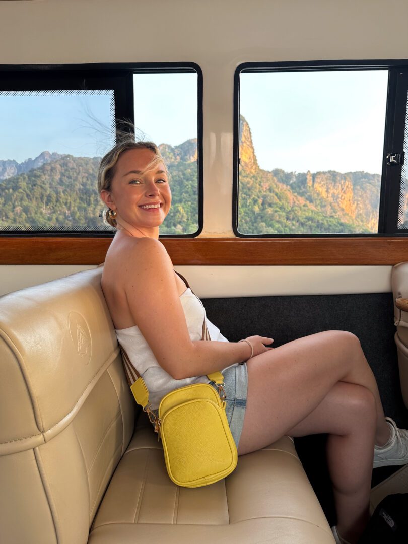 Smiling woman riding a speedboat transfer to Rayavadee Resort, with limestone cliffs of Railay Beach glowing in the golden hour through the window.