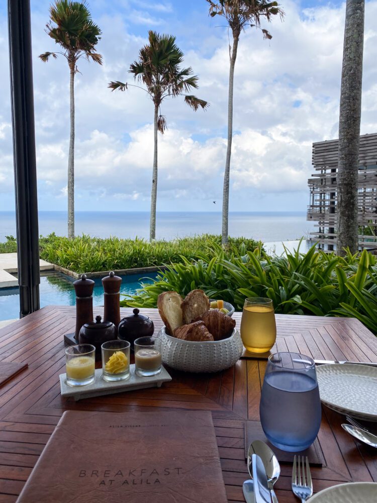 Scenic oceanfront breakfast at CIRE restaurant in Alila Villas Uluwatu, featuring fresh pastries and tropical juice with panoramic views of the Indian Ocean and minimalist Balinese architecture.