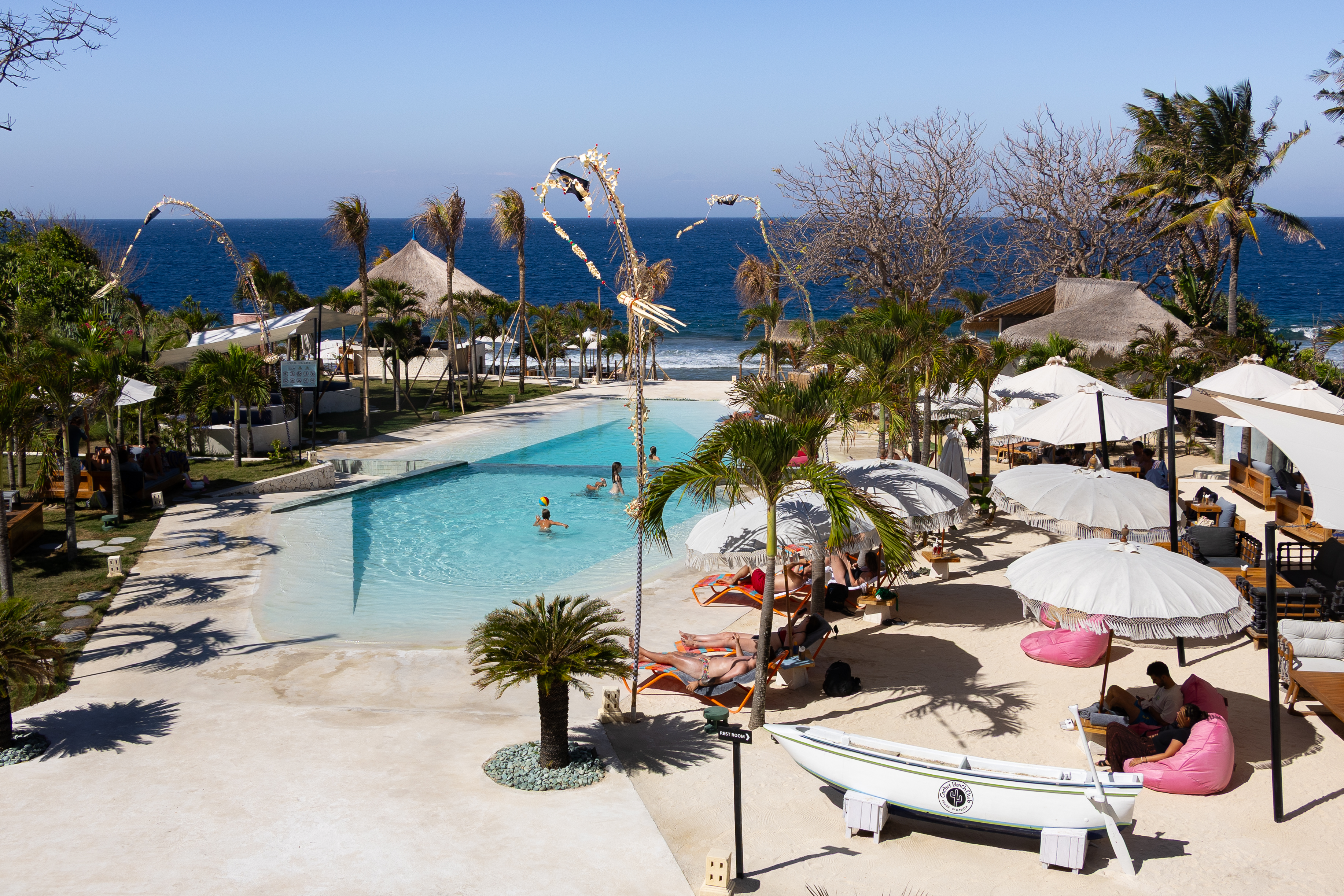 Beachfront pool scene at Cactus Beach Club on Nusa Penida, with sunbathers, umbrellas, and ocean views under clear blue skies.