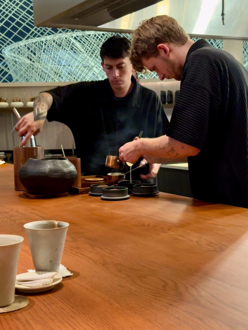 Two chefs carefully plate dishes behind the counter at ORE Bangkok, an intimate dining experience known for its creative tasting menu and modern minimalist aesthetic.