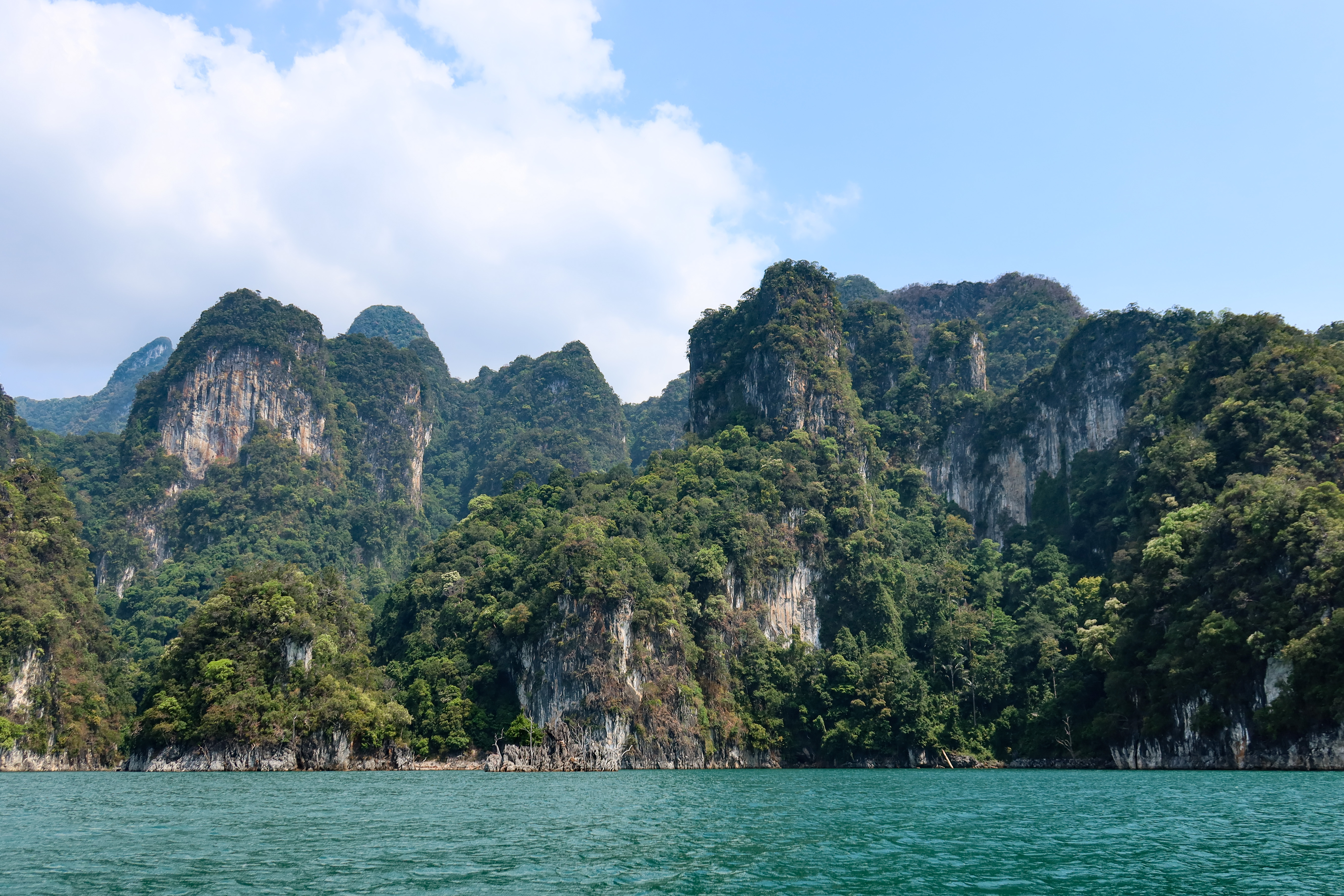Limestone cliffs blanketed in lush jungle rise dramatically from the emerald waters of Cheow Lan Lake in Khao Sok National Park, Thailand.