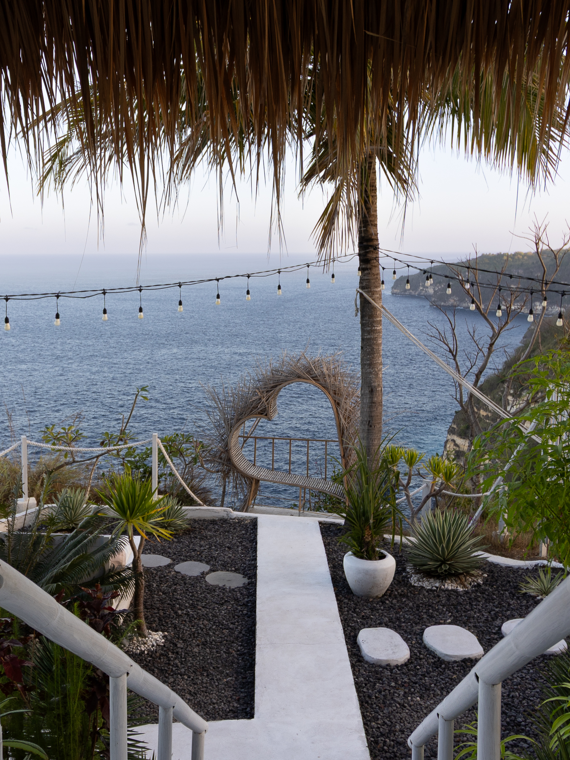 Romantic heart-shaped bamboo bench on a cliffside glamping retreat in Nusa Penida, with panoramic ocean views and tropical landscaping.