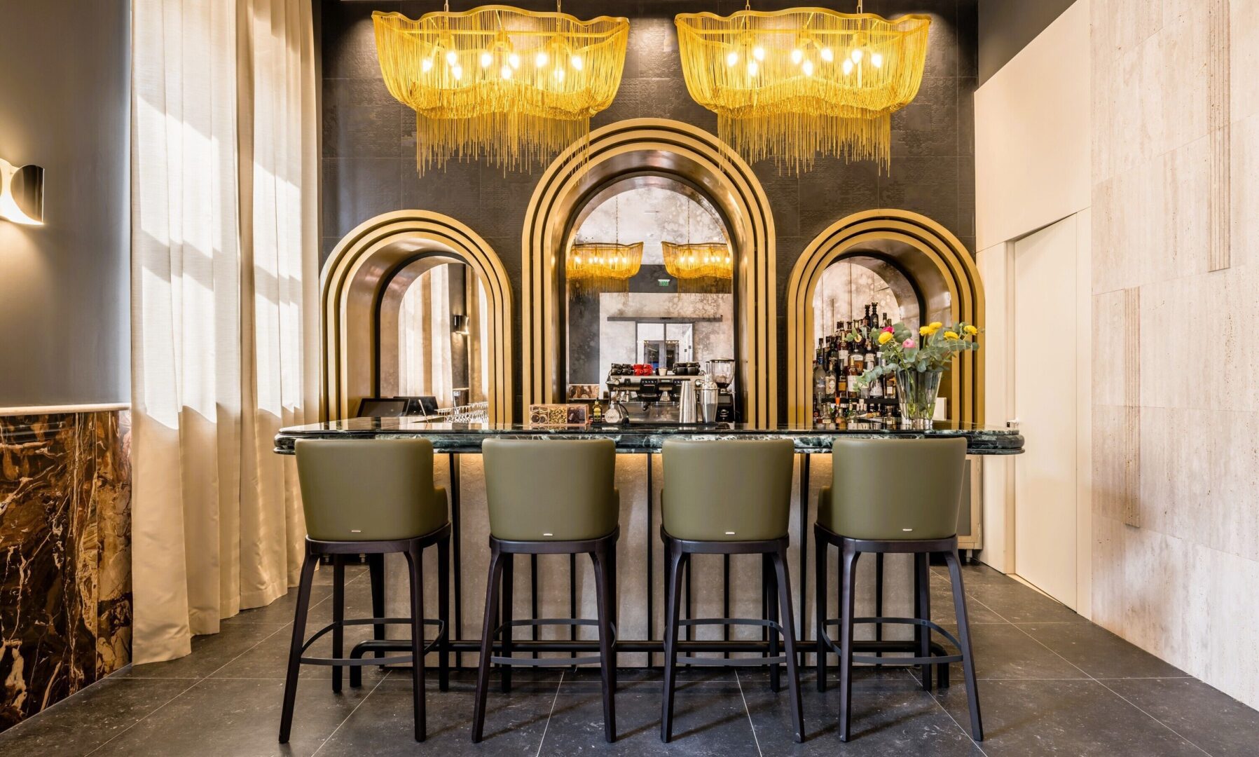 Stylish hotel in Split Croatia's bar featuring art deco arches, golden chandeliers, and a polished marble counter with modern bar stools.