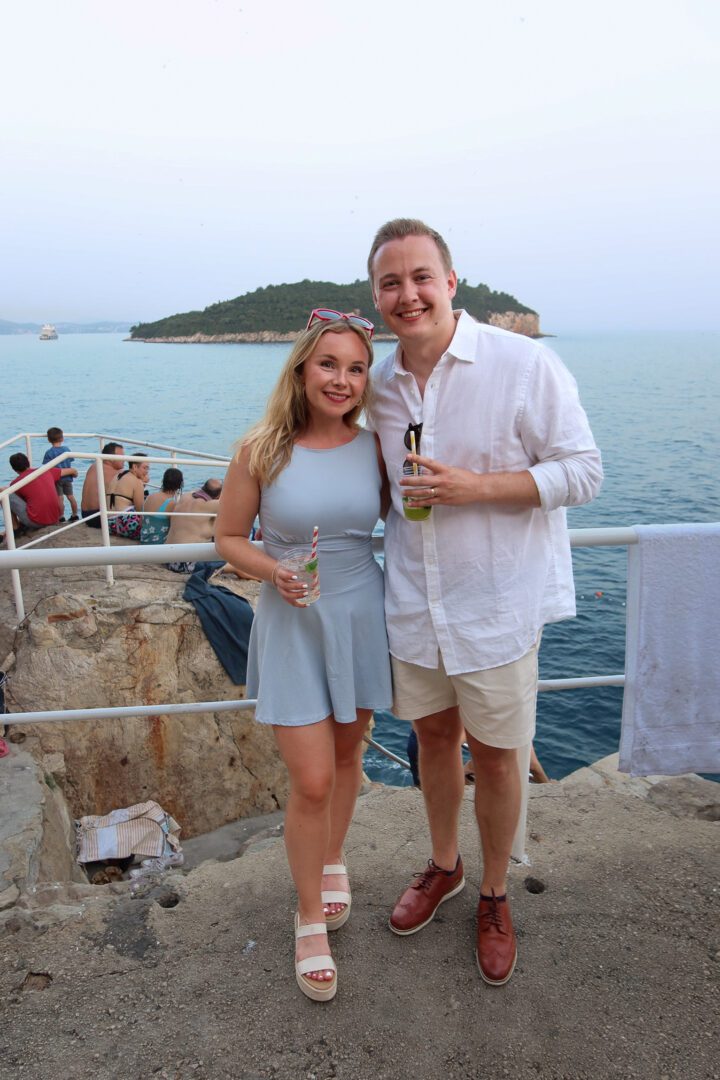 Couple enjoying sunset cocktails at Buža Bar, perched on the cliffs outside Dubrovnik’s city walls with views of Lokrum Island.