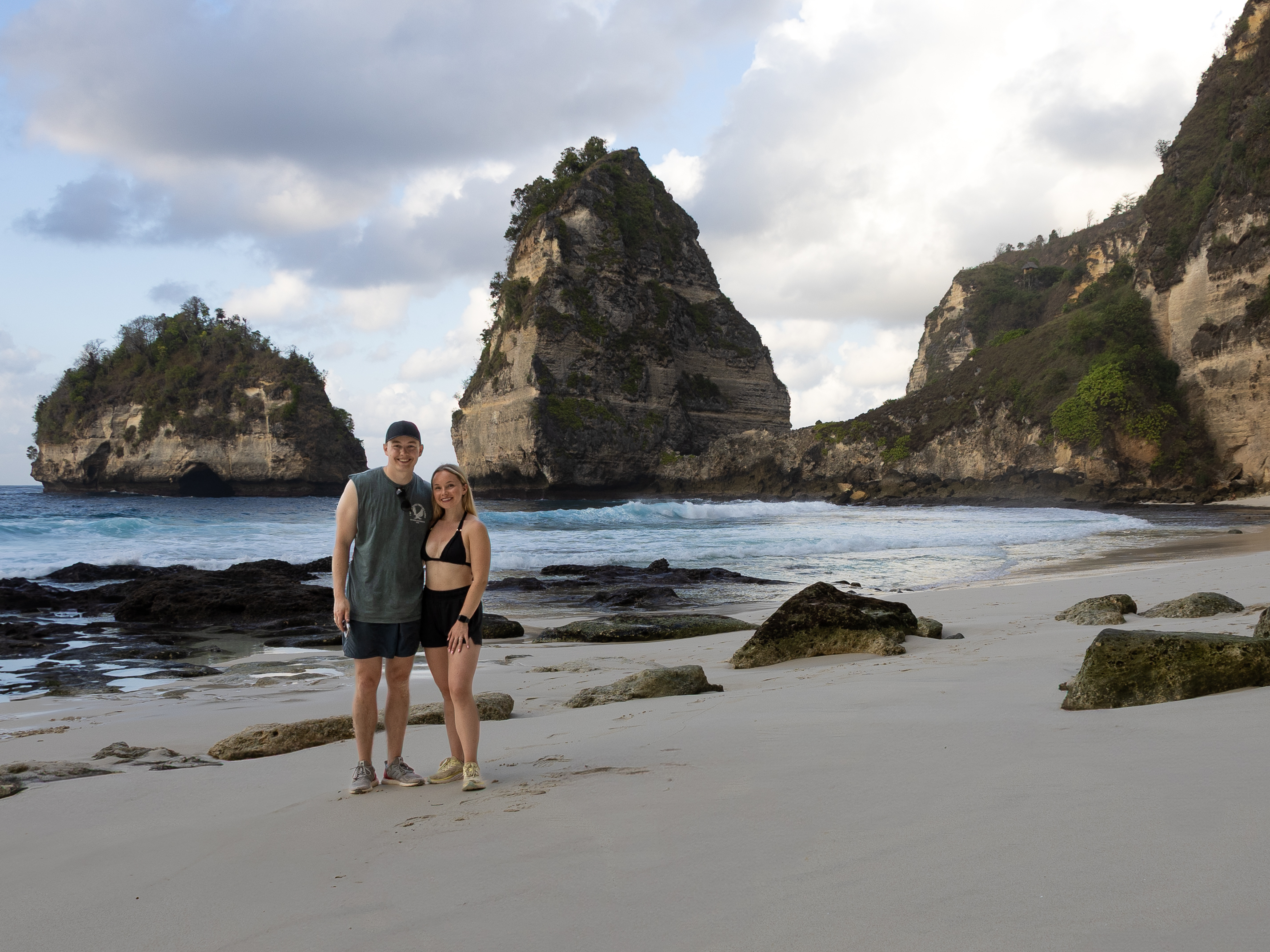 Couple standing on the white sands of Diamond Beach in Nusa Penida, surrounded by dramatic cliffs and turquoise waves.