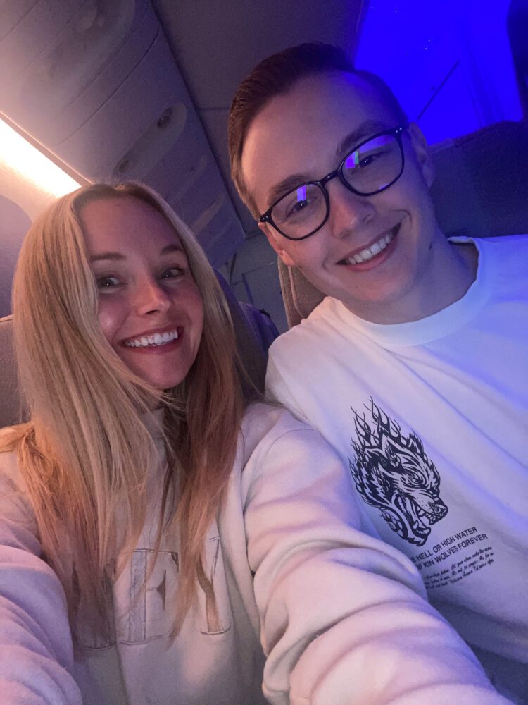 Happy couple taking a selfie under soft blue cabin lighting during an Emirates flight en route to Dubai.