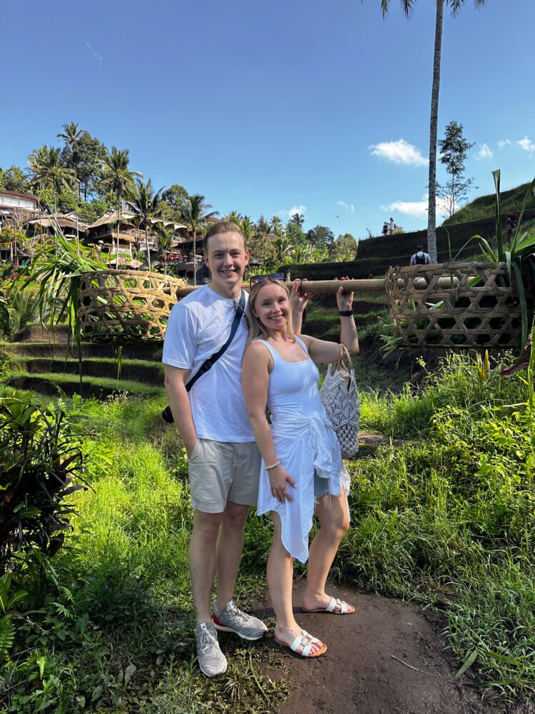 Smiling couple posing with a traditional woven basket amid the vibrant greenery and stepped landscape of Bali’s Tegalalang Rice Terrace.