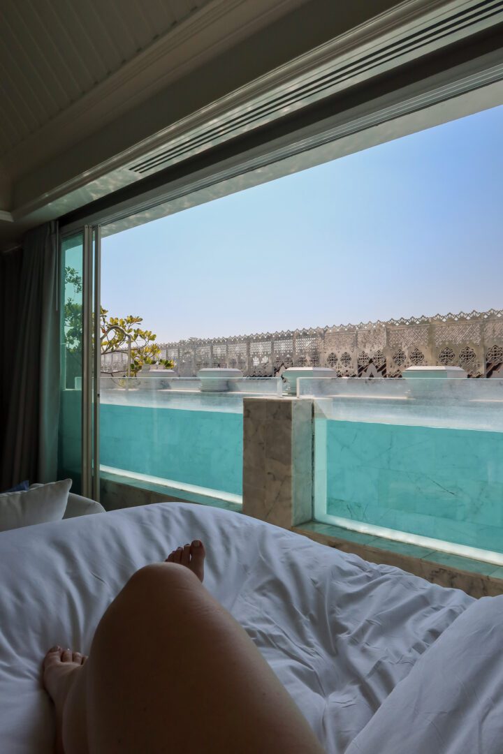 Relaxing poolside suite at Inside House in Chiang Mai, with legs stretched out on a bed and a serene private pool just outside the open sliding glass doors.