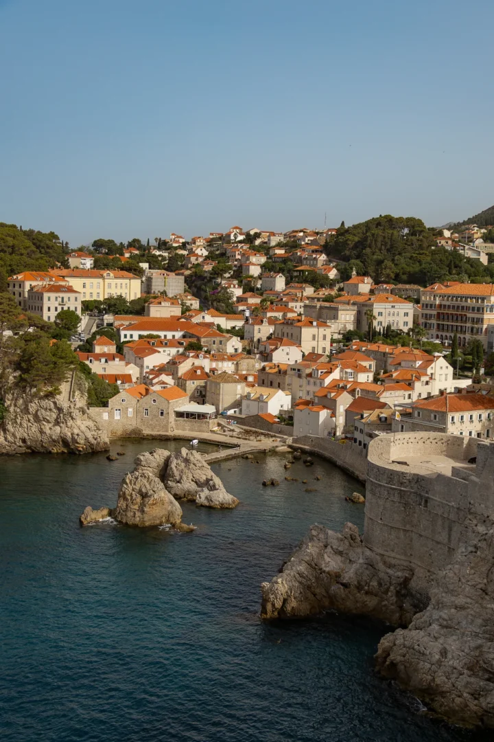 Golden-hour view of Dubrovnik’s coastal neighborhood and rocky inlet, captured from the city walls with warm light illuminating the terracotta rooftops.
