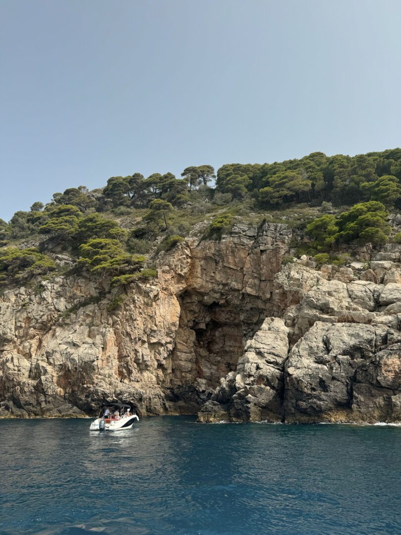 White speedboat anchored by dramatic cliffs and sea caves along the Elaphiti Islands’ rugged coastline.