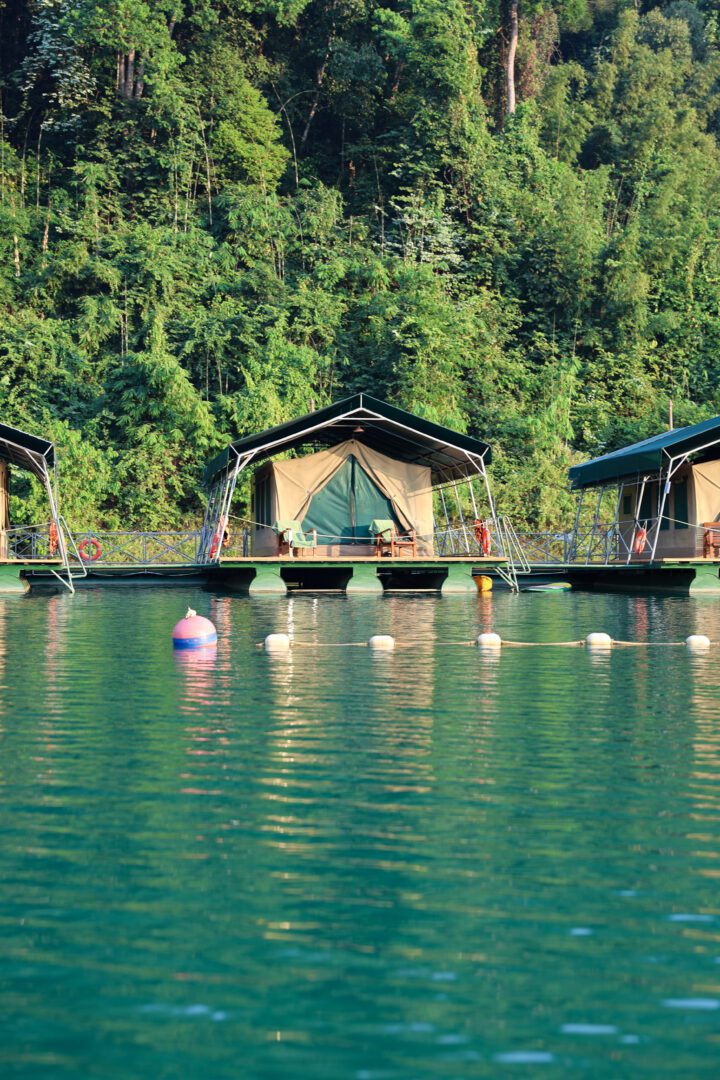 Luxury safari-style tents float serenely on the emerald waters of Cheow Lan Lake at Elephant Hills Lake Camp, backed by dense jungle in Khao Sok National Park.