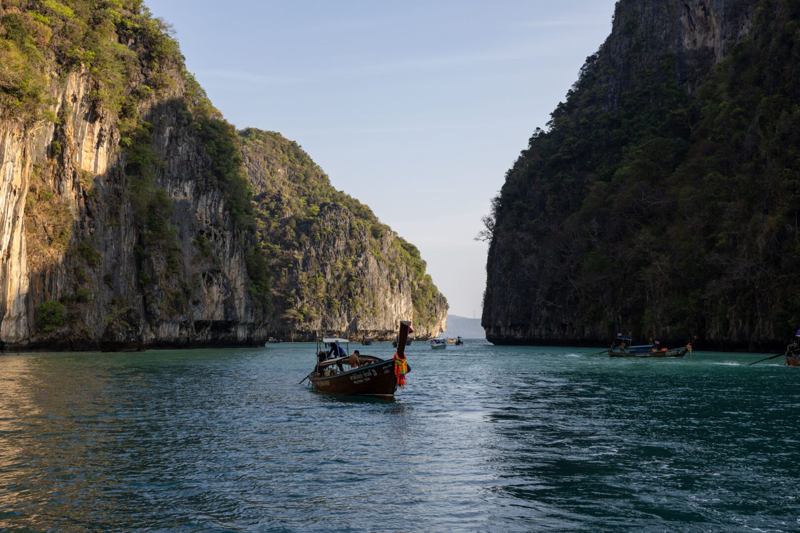Longtail boat cruising through the emerald waters of Pileh Lagoon, surrounded by steep limestone cliffs on Koh Phi Phi Leh.