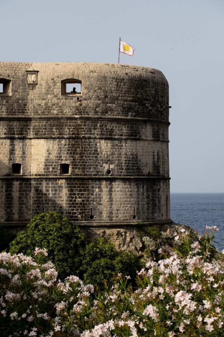 Fort Bokar’s rounded stone walls overlook the sea, framed by blooming flowers along Dubrovnik’s city walls.