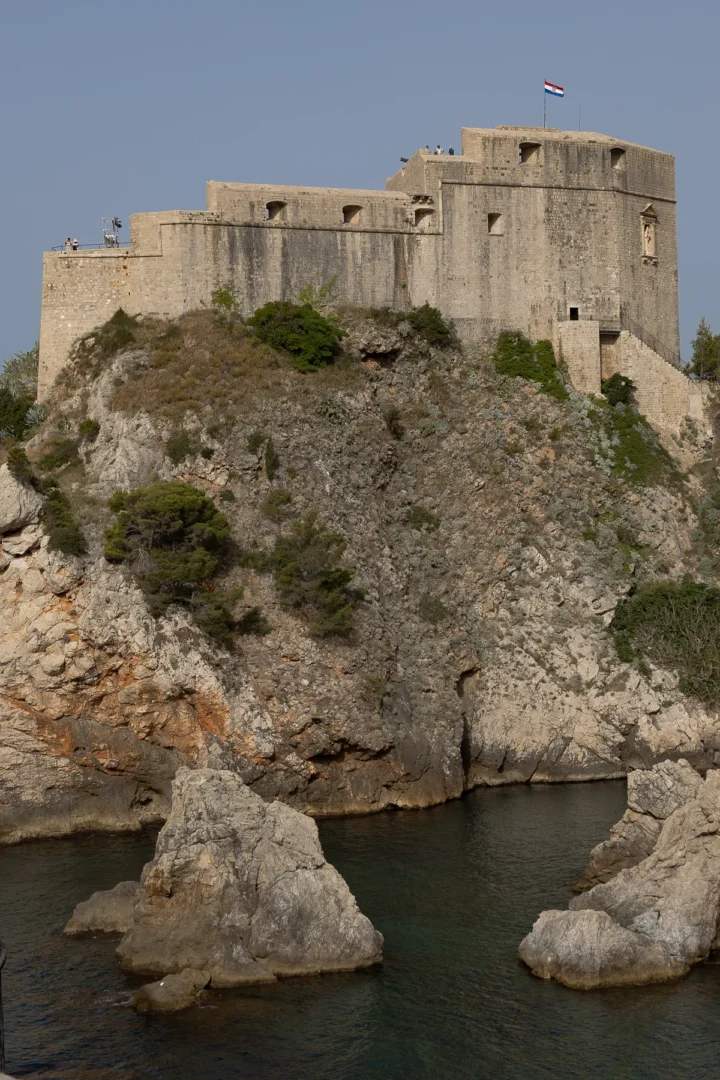 Close-up view of Fort Lovrijenac rising above rugged cliffs and turquoise waters, with the Croatian flag flying proudly atop the fortress.