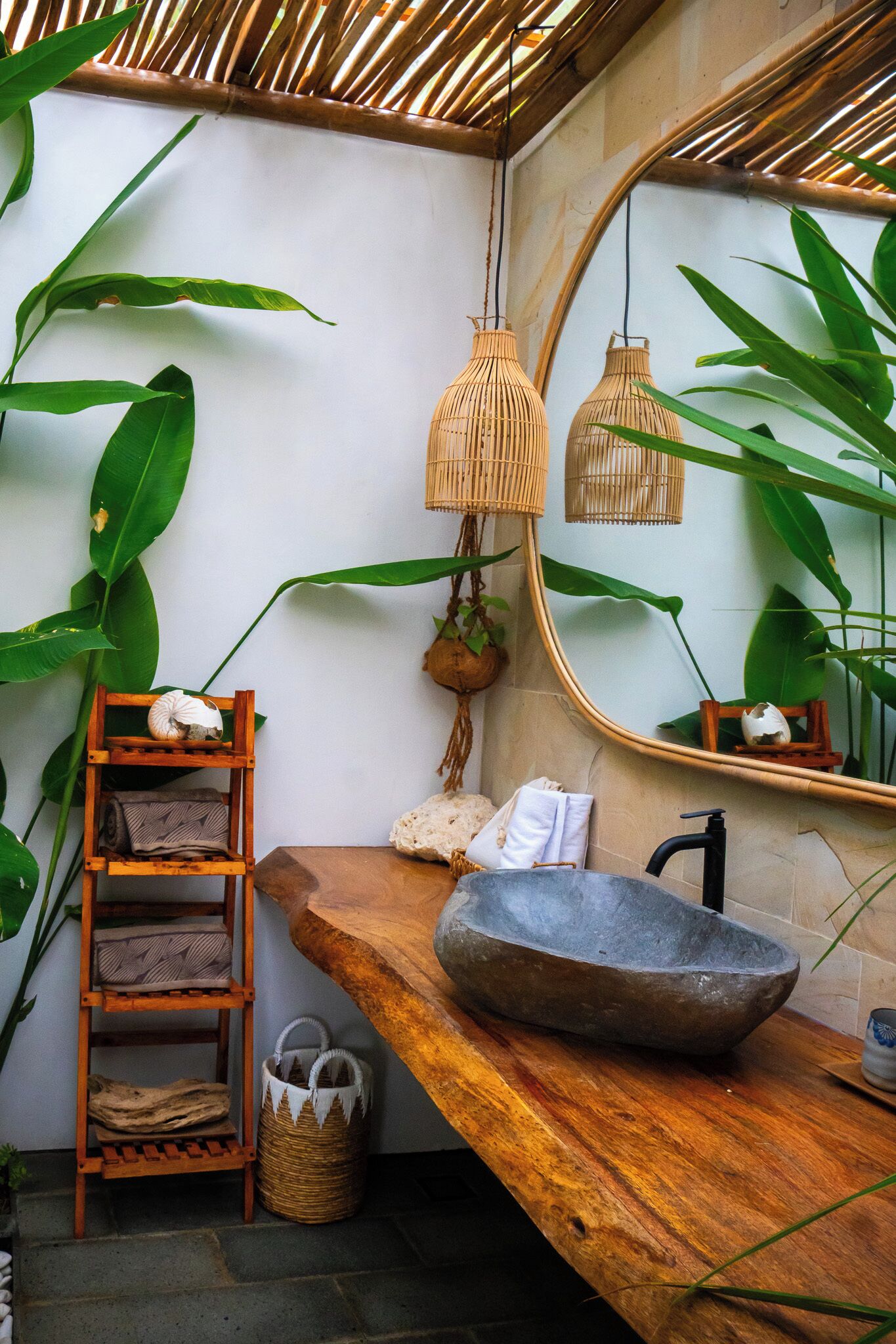 Tropical-inspired bathroom at Gamat Bay Resort, featuring a stone basin sink, natural wood counter, lush greenery, and woven accents for a serene open-air feel.