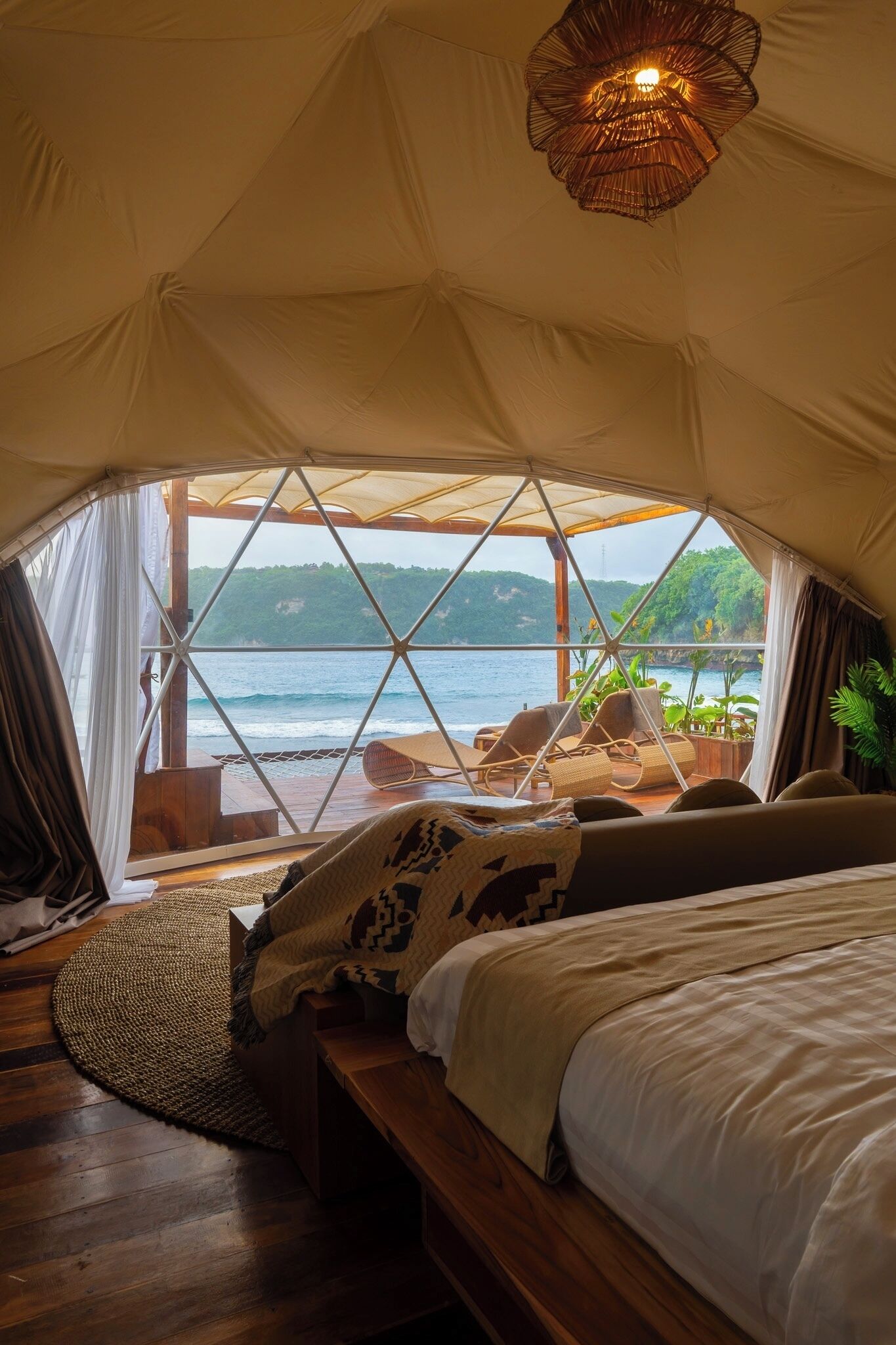 Inside a luxury dome villa at Gamat Bay Resort, featuring ocean views, cozy earth-toned decor, and a private deck with sun loungers overlooking the waves.
