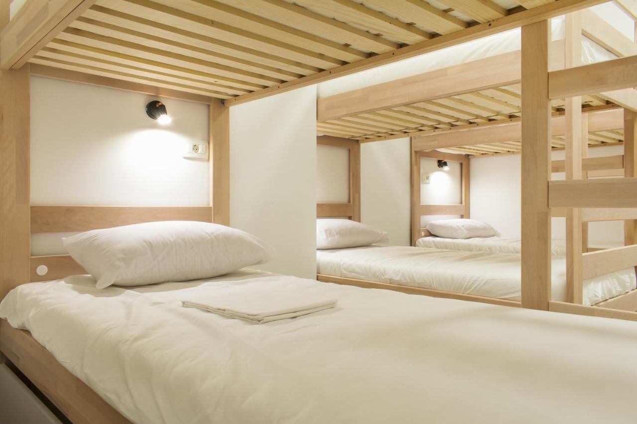 Minimalist dormitory with light wood bunk beds and individual reading lamps for a cozy, modern stay in one of the more affordable hotels in Split Croatia.