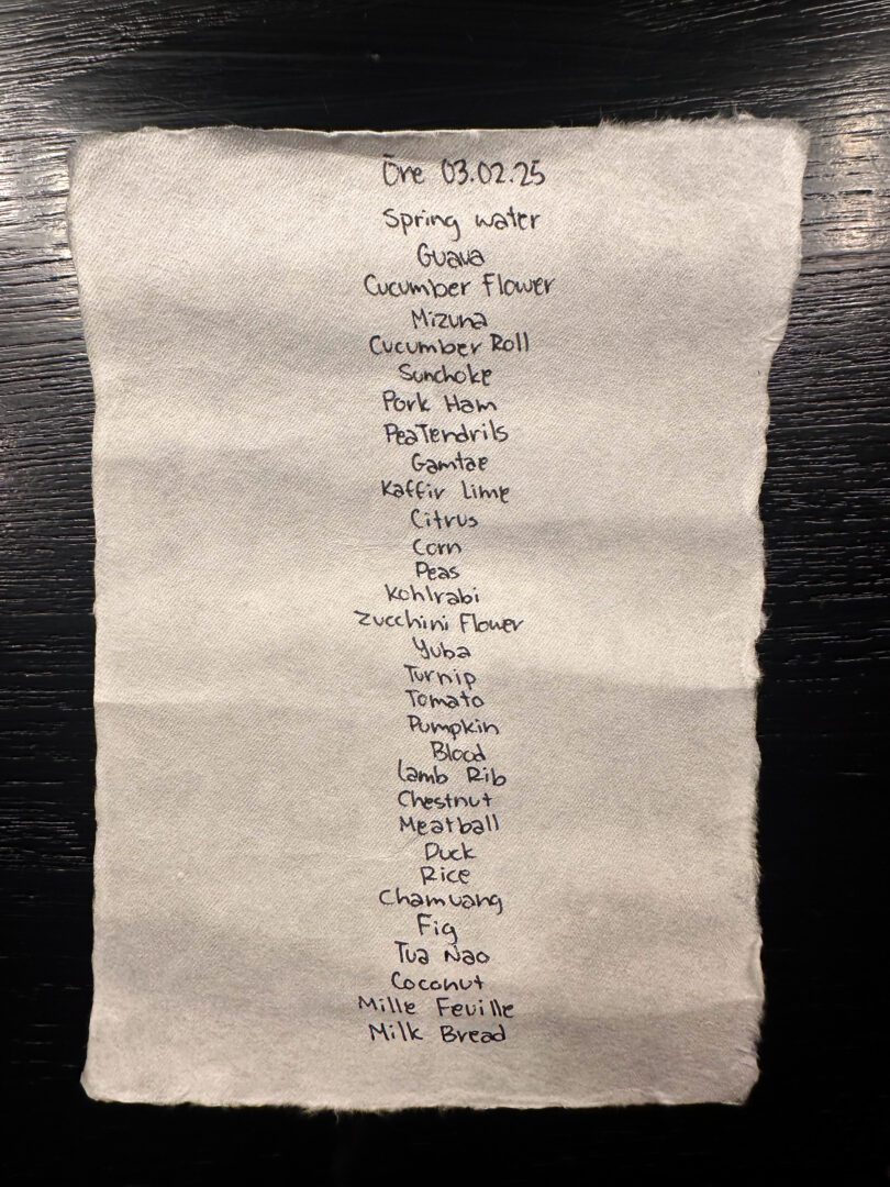 A hand-written tasting menu on cloth at ORE Bangkok showcases an inventive progression of seasonal ingredients, including guava, sundoke, pork ham, lamb rib, and mille-feuille.