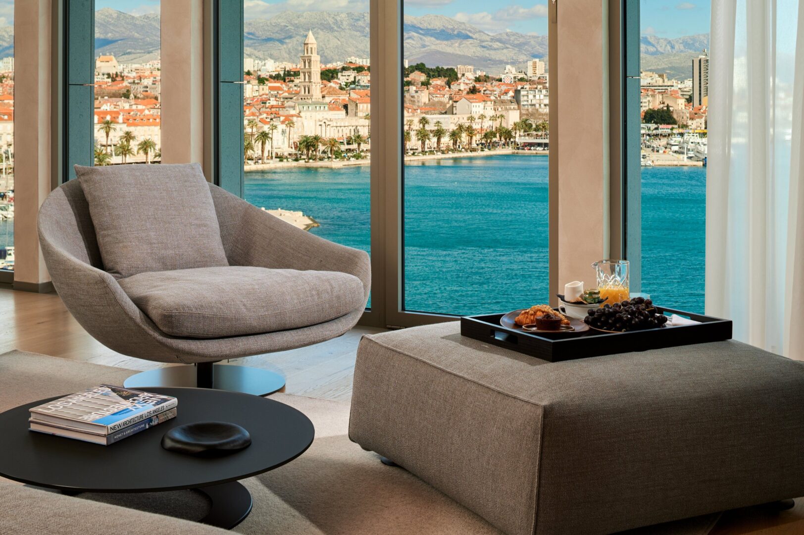 Modern hotel room lounge area with sweeping floor-to-ceiling views of Split Croatia's Old Town, Riva promenade, and the Adriatic Sea.