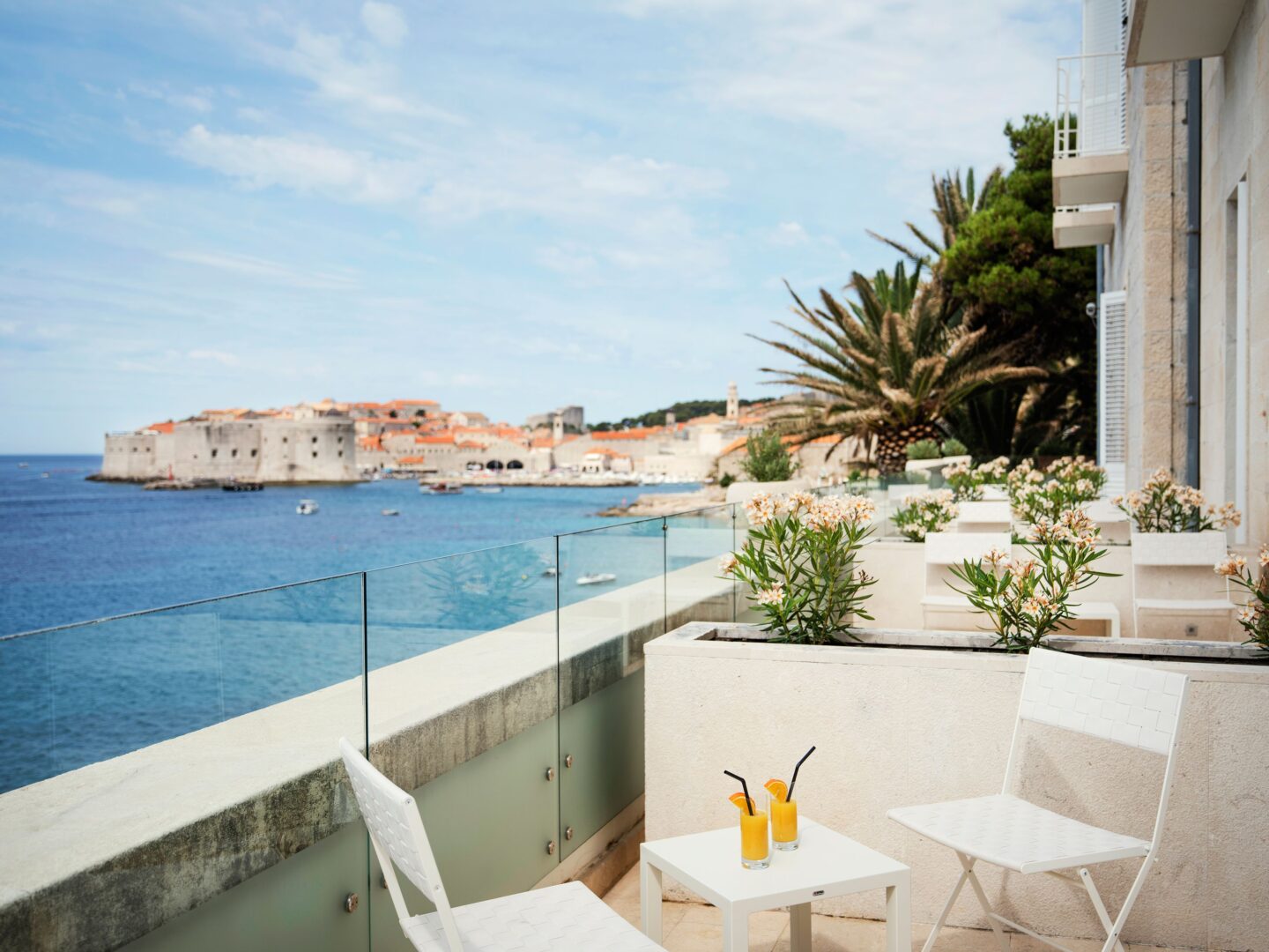 Sunny terrace at Hotel Excelsior Dubrovnik with white patio seating, fresh orange juice, and spectacular views of the Adriatic and Dubrovnik’s historic Old Town and city walls.