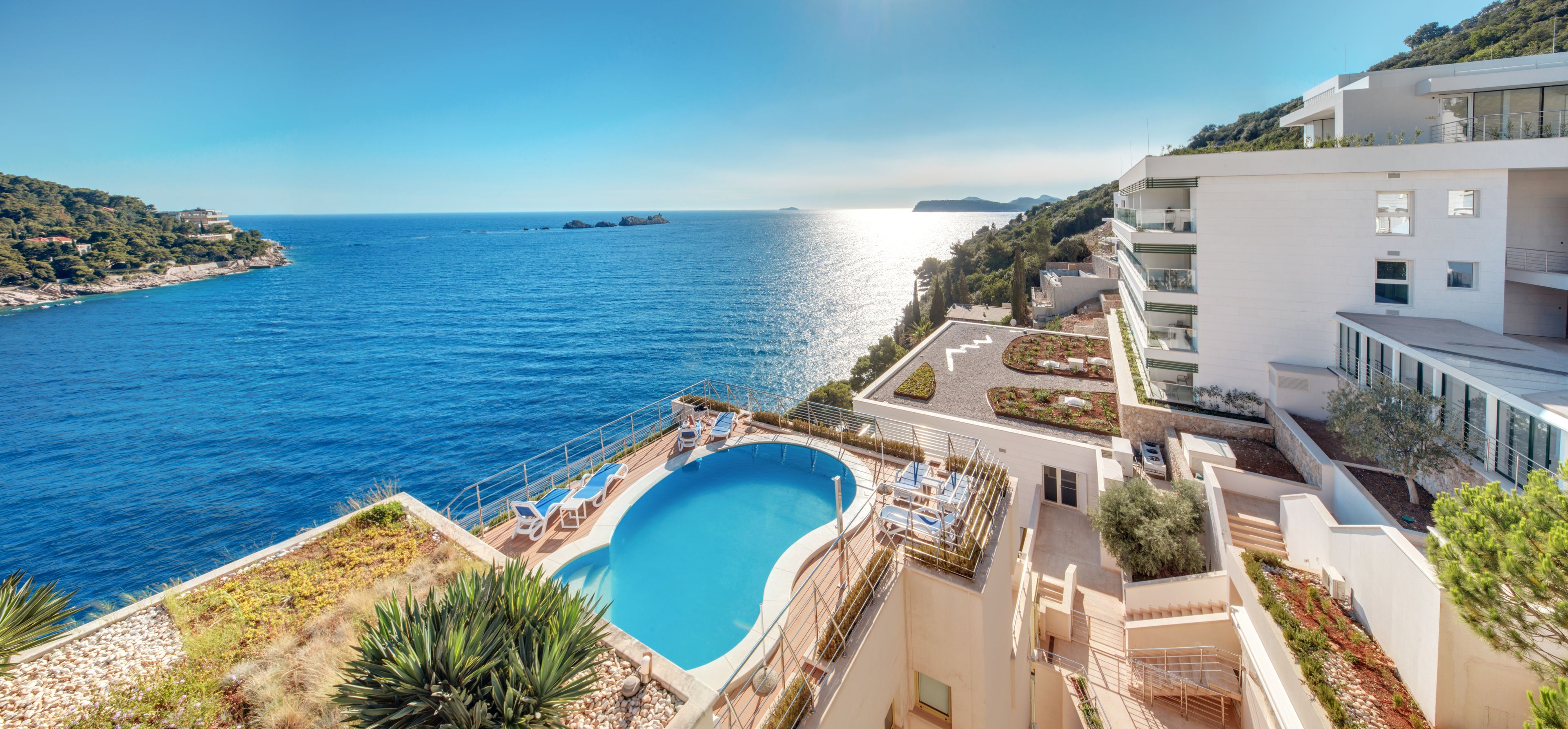 Stunning clifftop pool at Hotel More Dubrovnik with panoramic views of the Adriatic Sea, surrounded by sun loungers and modern white architecture cascading down the hillside.