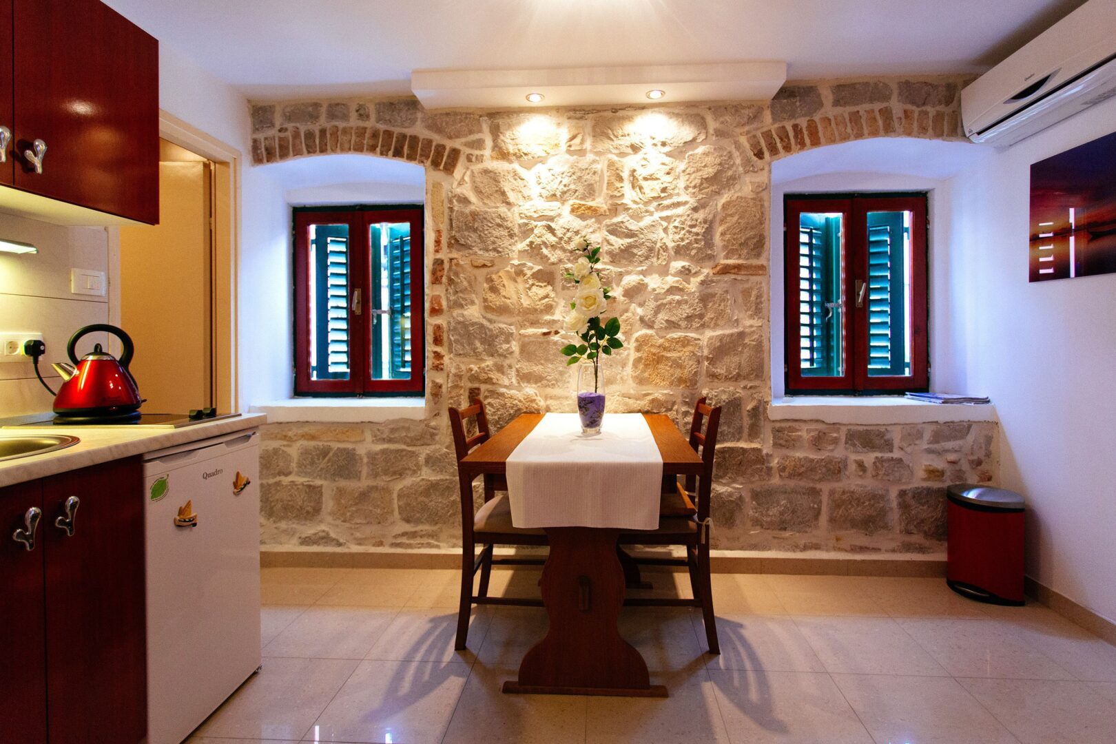 Rustic apartment interior with a cozy dining table, stone walls, and a compact kitchen featuring modern amenities.