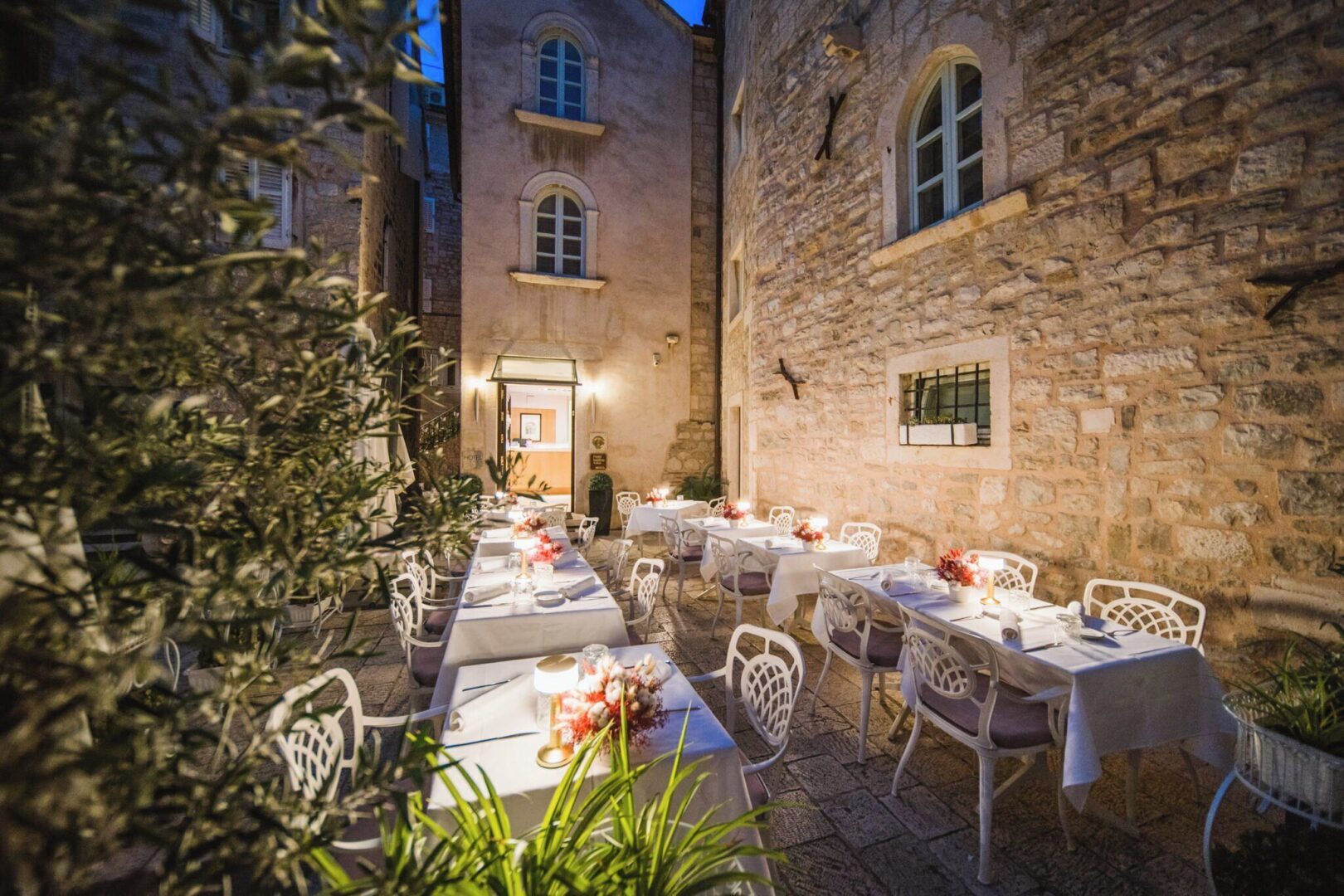 Romantic outdoor hotel dining courtyard surrounded by ancient stone walls, softly lit under the evening sky in Split, Croatia.