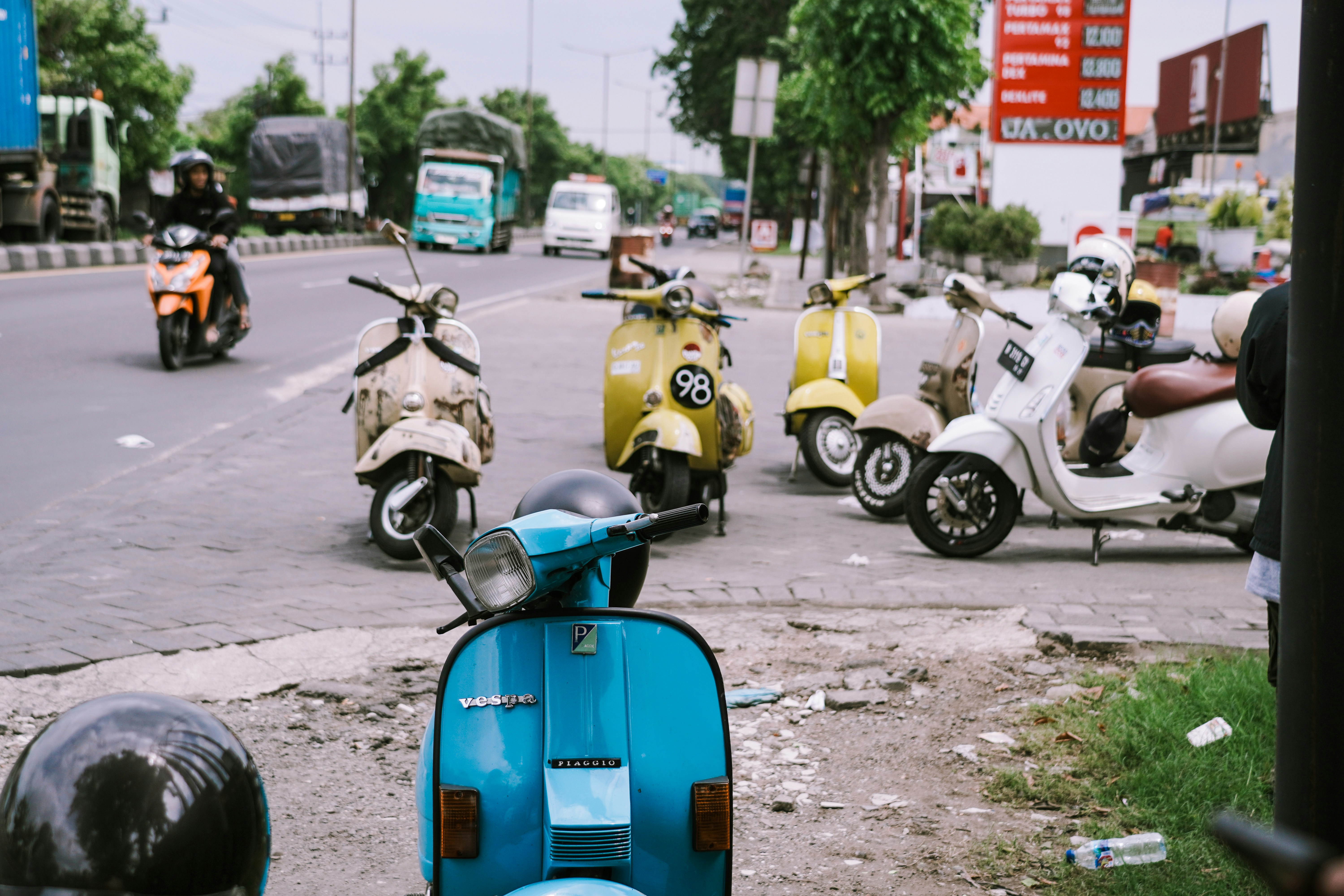 Colorful vintage scooters parked along a busy roadside in Indonesia, with trucks and motorbikes passing by in the background.