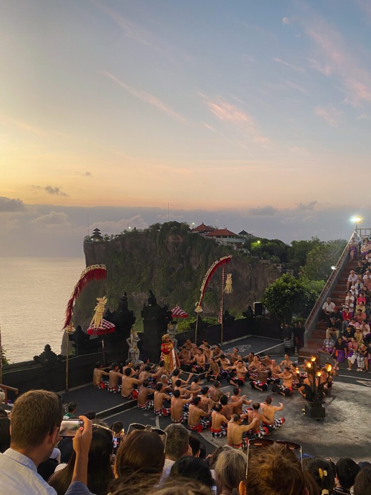 Evening performance of the Kecak Fire Dance at Uluwatu Temple, with a dramatic cliffside ocean view and a glowing sunset sky.