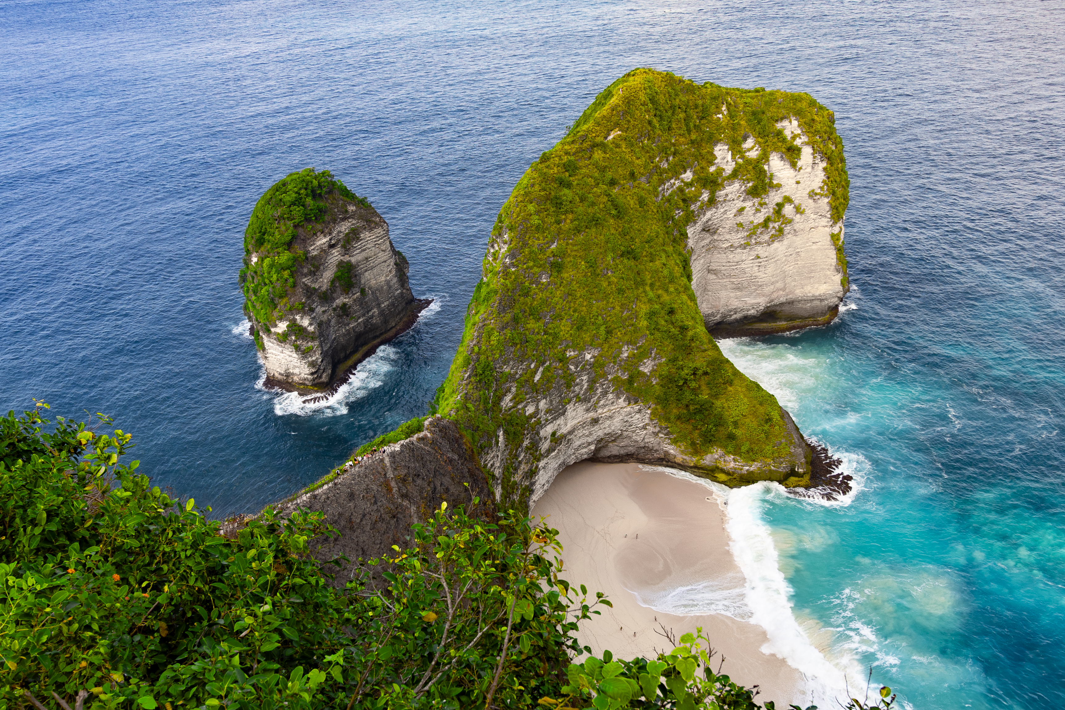 Iconic aerial view of Kelingking Beach on Nusa Penida, with its dinosaur-shaped cliff and turquoise waves crashing onto the secluded white sand below.