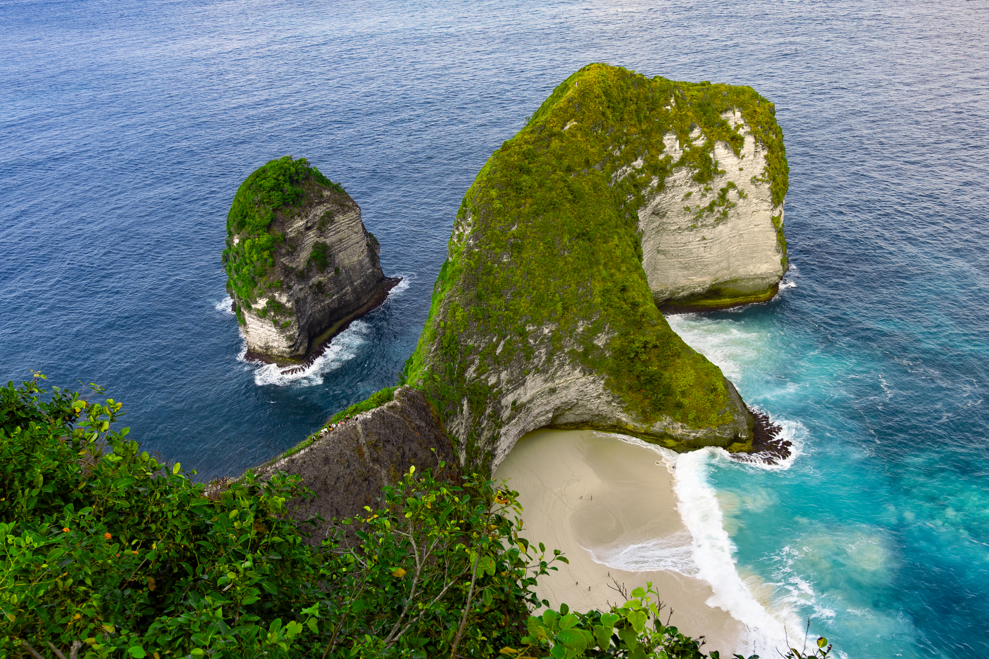 Iconic aerial view of Kelingking Beach on Nusa Penida, with its dinosaur-shaped cliff and turquoise waves crashing onto the secluded white sand below.