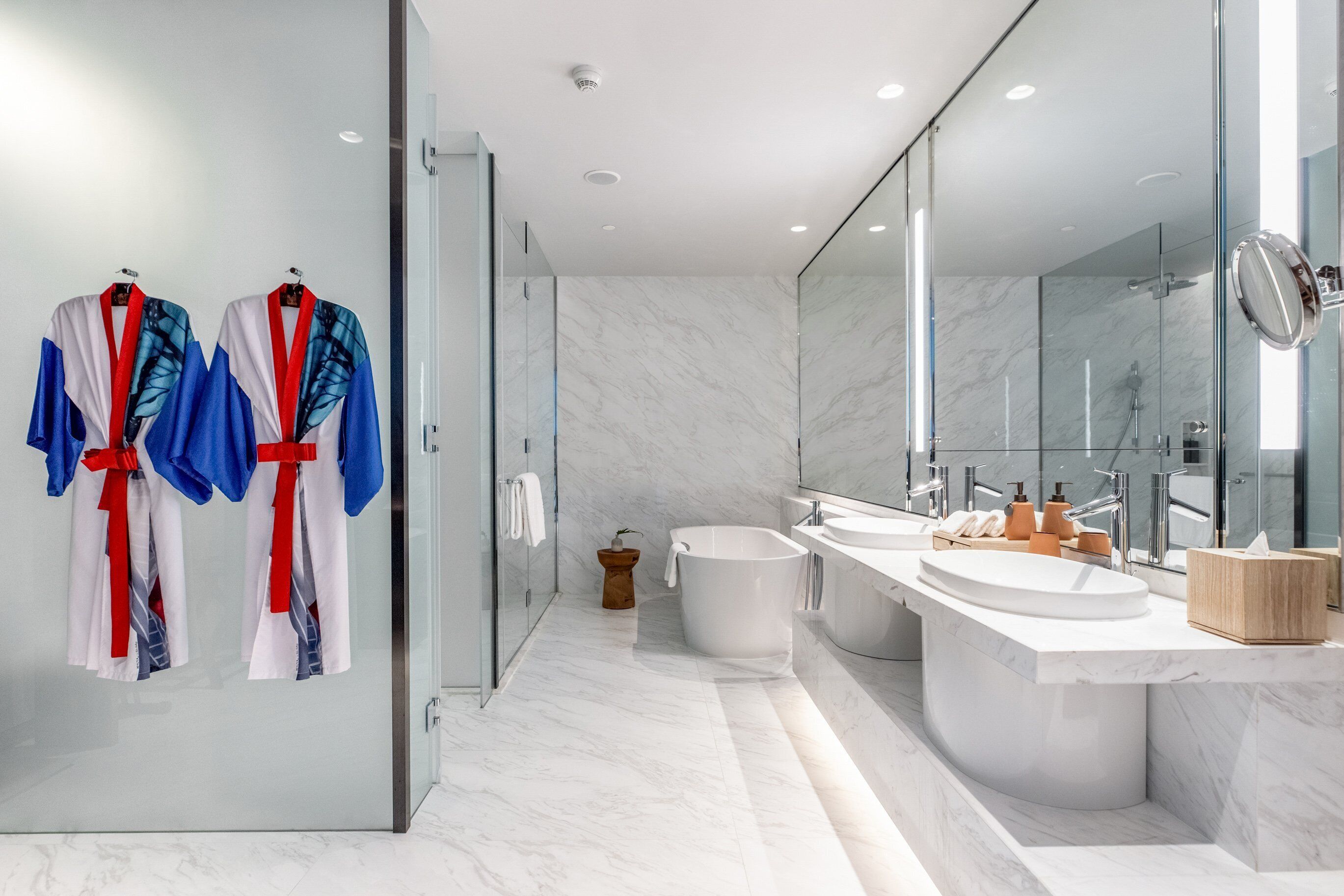Sleek marble bathroom at Kimpton Maa-Lai Bangkok featuring double sinks, a modern soaking tub, and colorful butterfly-inspired robes adding a bold pop of color to the minimalist design.