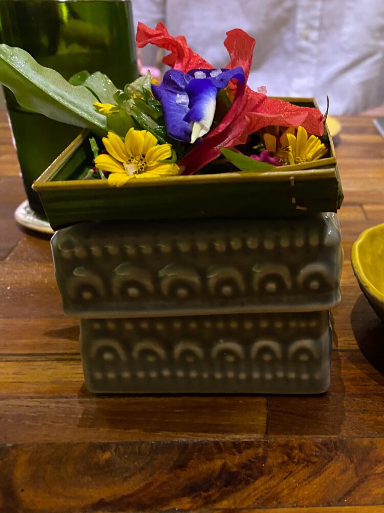 A beautifully presented dish at Locavore Bali, inspired by traditional Hindu offerings and garnished with colorful edible flowers in a woven leaf basket.