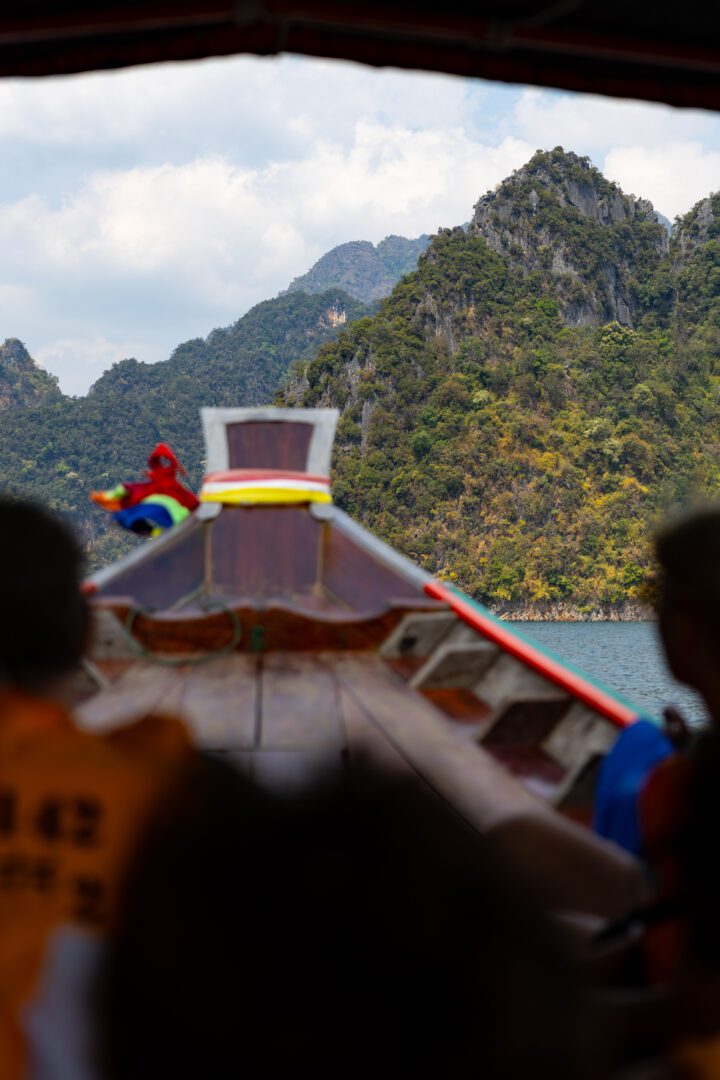 Passengers aboard a traditional longtail boat cruise through the scenic limestone peaks and emerald waters of Cheow Lan Lake in Khao Sok National Park.