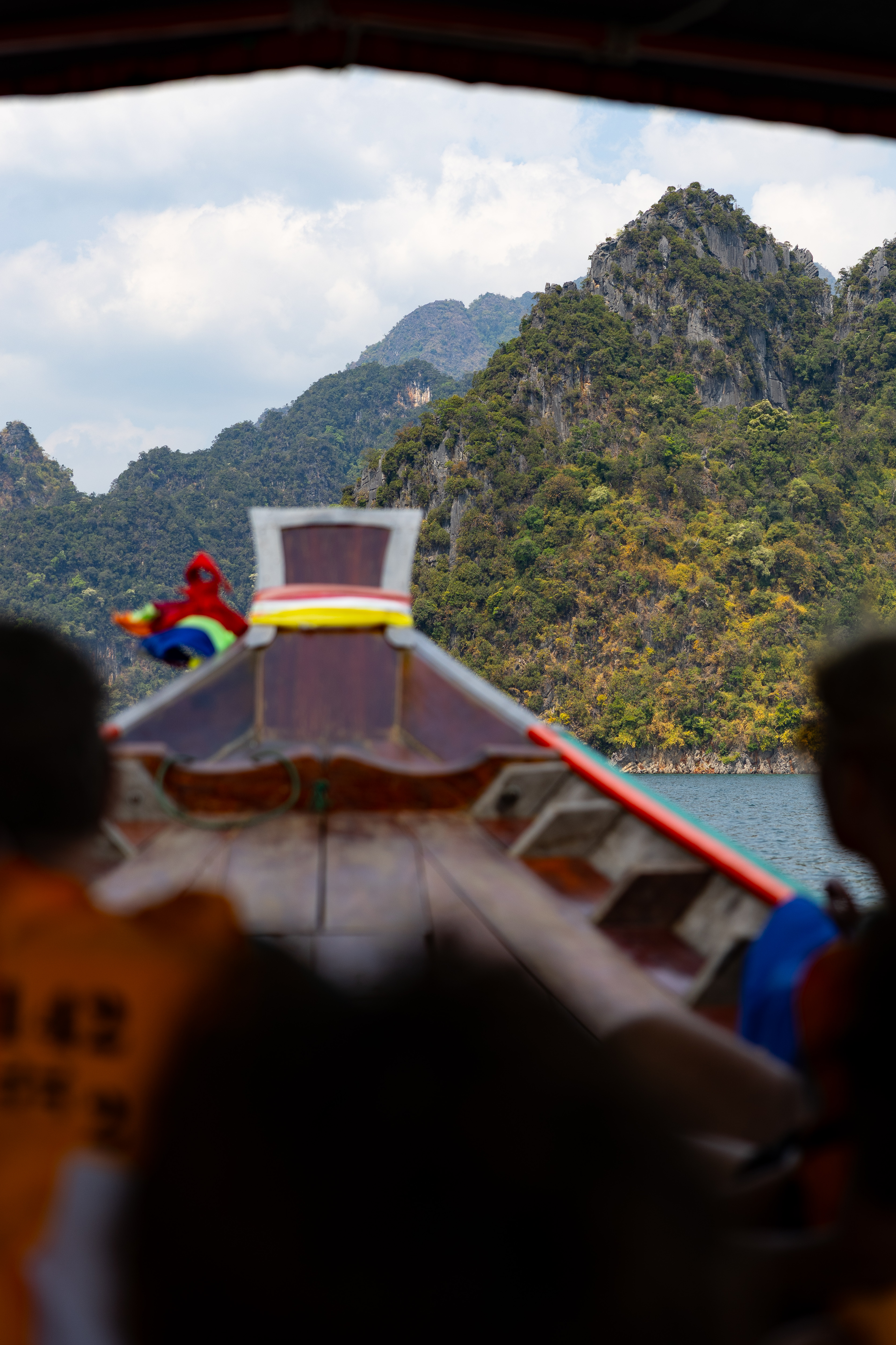 Passengers aboard a traditional longtail boat cruise through the scenic limestone peaks and emerald waters of Cheow Lan Lake in Khao Sok National Park.