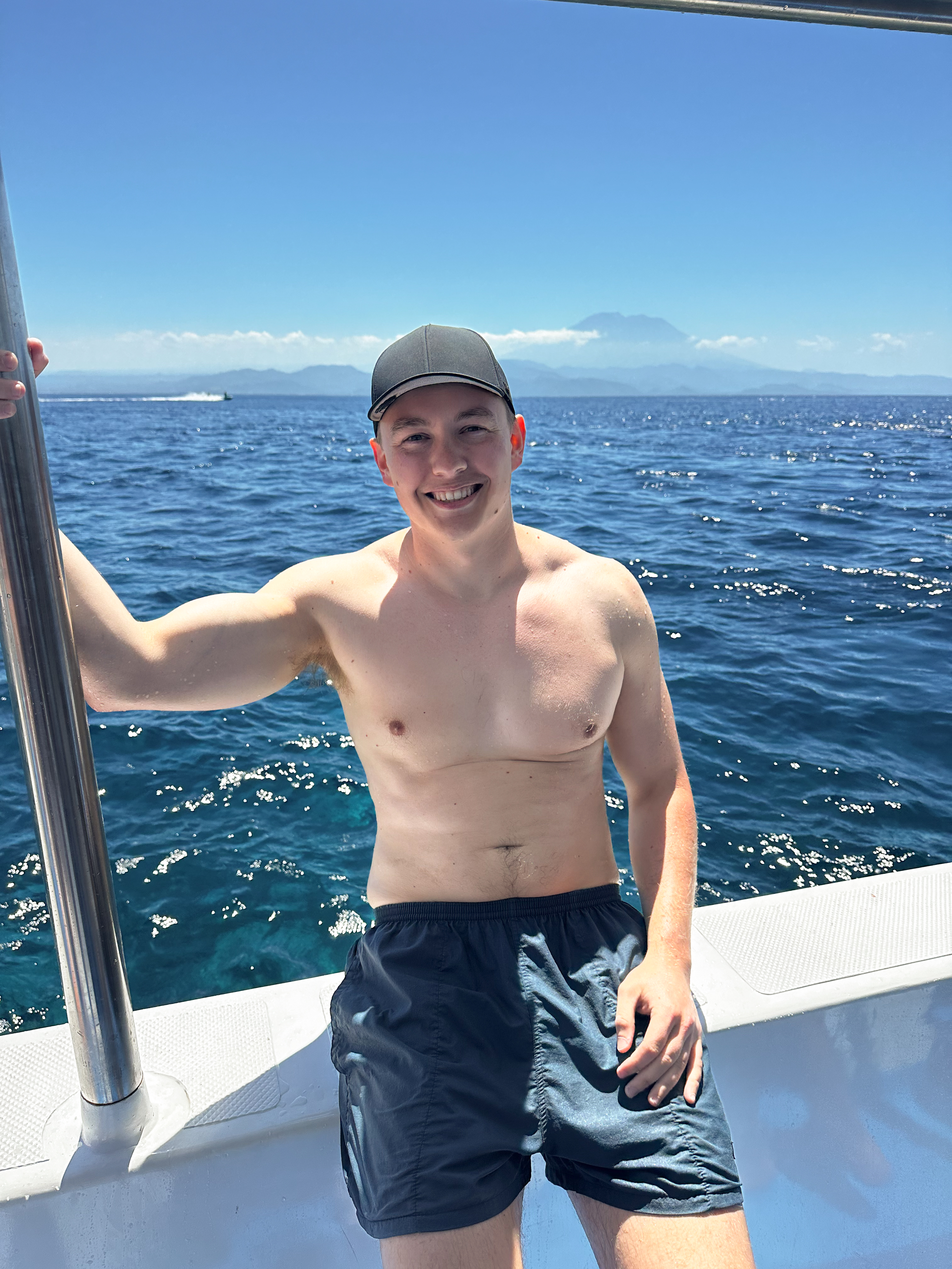 Man smiling on a snorkeling boat off the coast of Nusa Penida, with the deep blue sea and Mount Agung in the background.