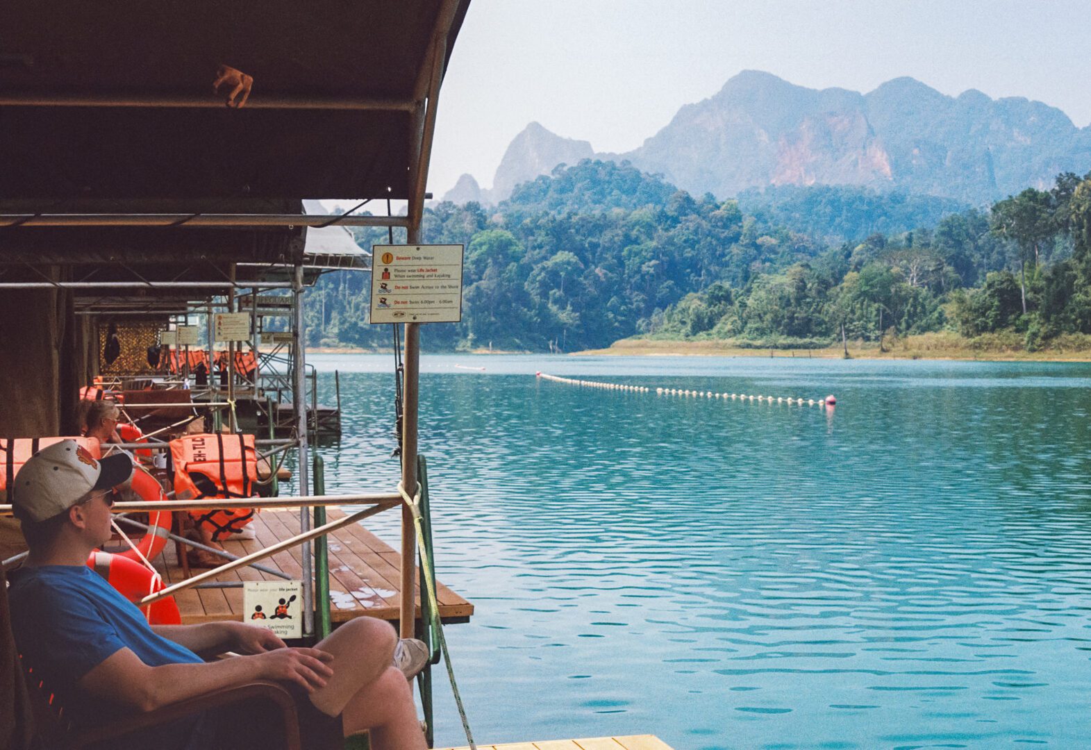 A man relaxes outside his floating tent at Elephant Hills Lake Camp, taking in the peaceful views of Cheow Lan Lake and the surrounding jungle-covered cliffs.