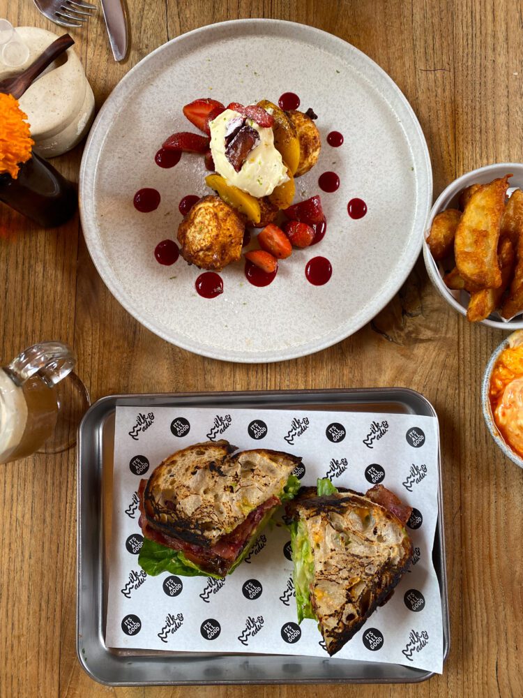 A delicious breakfast spread featuring peach-topped French toast, BLT sandwich, and crispy potato wedges at Milk & Madu in Bali.