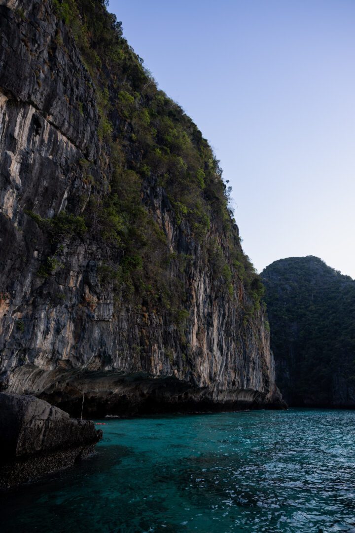Sheer limestone cliffside rising above emerald waters near the entrance to Maya Bay on Koh Phi Phi, captured in the soft light of morning.