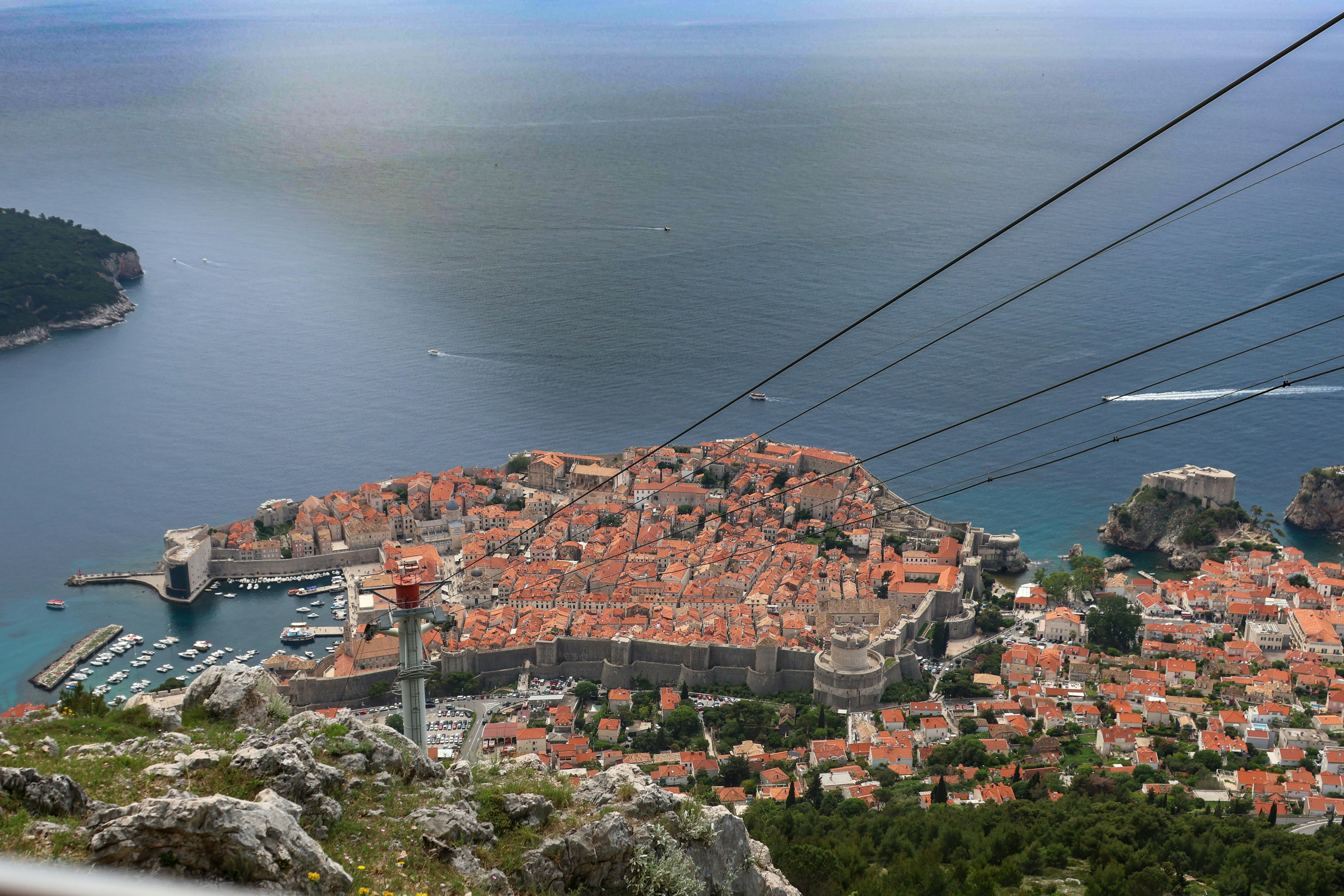 Panoramic view of Dubrovnik’s Old Town and surrounding coastline as seen from Mount Srđ, with cable car lines stretching overhead.