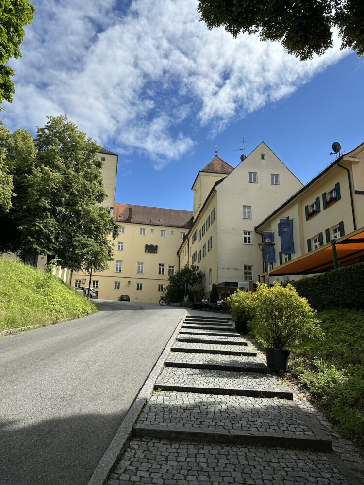 Exterior view of the historic Weihenstephan Brewery in Freising, Germany—the world’s oldest brewery—featuring traditional Bavarian architecture, ivy-covered brick walls, and a scenic hilltop location under a blue sky.